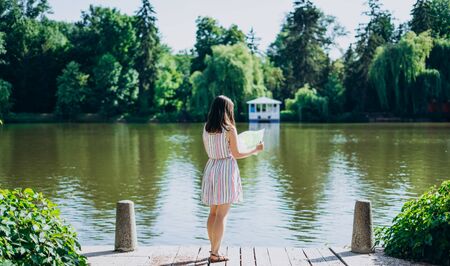 Sofia Park, Uman. Young woman with a tourist map by the lake. A woman in a colored dress walks along the river. Girl on a background of a white gazebo near the lakeの写真素材