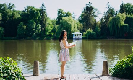 Sofia Park, Uman. Young woman with a tourist map by the lake. A woman in a colored dress walks along the river. Girl on a background of a white gazebo near the lakeの写真素材