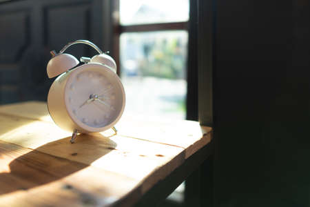 White alarm clock placed on a wooden tableの写真素材
