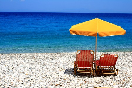 Chairs and an umbrella sit calmly on a beach in Greece while waves lap at the shore. の写真素材