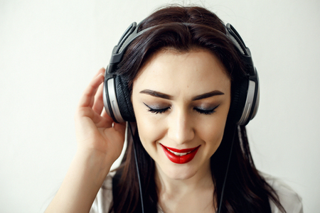 Happy pretty smiling woman with red lips listens to music in headphones over white backgroundの写真素材