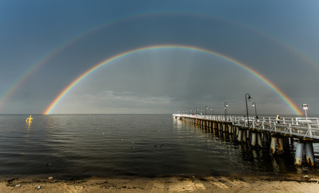 Blue sky and a rainbow over small sandy stream on beachの写真素材