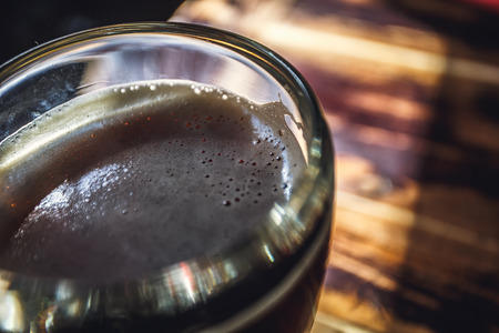 Glass of beer on brown wooden table over dark background. Glass of beer on a table.