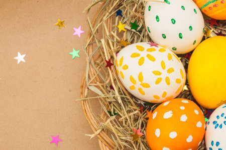 colored easter eggs in basket with hay and kraft background