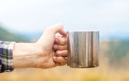 Metal touristic tea cup in man hand on outdoor backgroundの写真素材