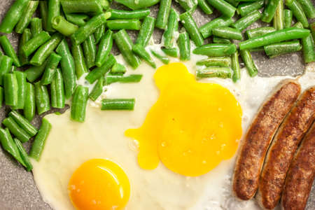 green beans with eggs and sausages on grey frying panの写真素材