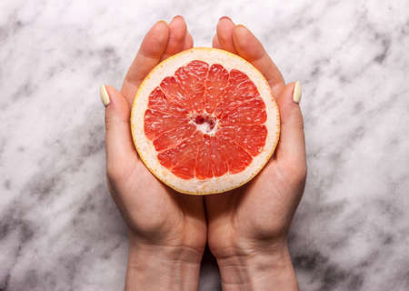 female hands keeping cut grapefruitの写真素材