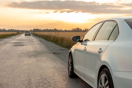 white car at sunset on country road next to yellow wheat field