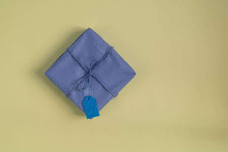 one craft violet paper wrapped gift with blue tag on yellow background. Flat lay. Copy spaceの写真素材