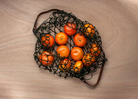 mandarins in green net bag zero waste concept lay on wooden tableの写真素材