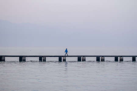 one kid walking along the pier over foggy lake background with copyspace