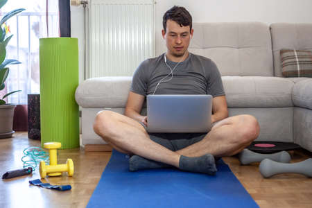 young man in mask on quarantine exercising and working at home with laptop and mobile phone