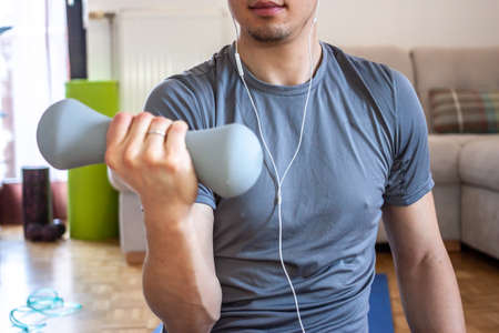 young man on quarantine exercising and working at home with mobile phone and  headphonesの写真素材