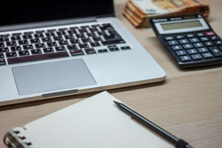 office table with laptop, notebook, calculator and cash stackの写真素材