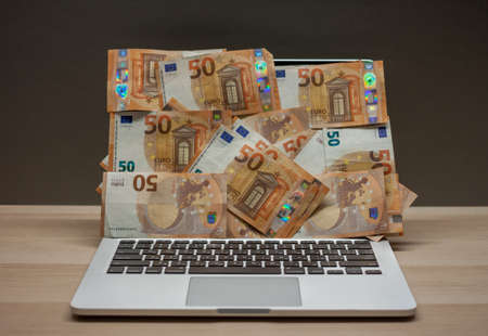 open laptop with screen covered by fifty euro banknotesの写真素材
