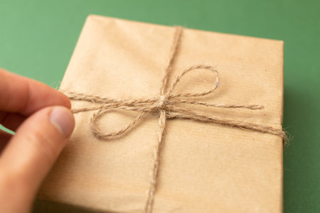 hand opening craft wrapped gift over green background