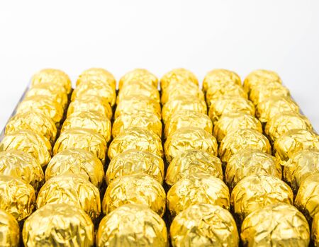 a lot of shiny golden chocolate wrapper in line on white background..