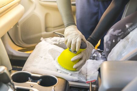 a man cleaning car interior by use foam chemical  and scrubbing machine.の写真素材