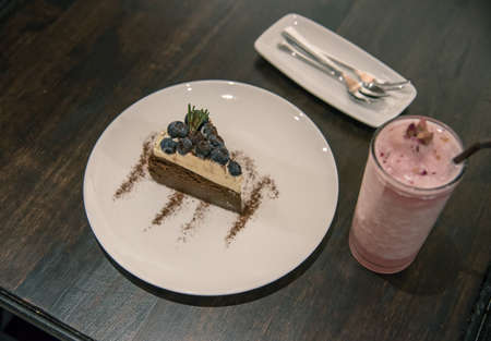 cheese cake topping with blueberry is a dessert for after dinner on the wood table with spoon and strawberry drinkの写真素材