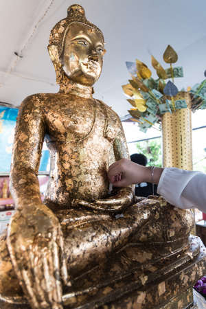 Hand with small gold plate are stick the gold at the buddha meaning for beautiful life.の写真素材