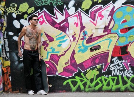 Young teen with tattoos with skateboards in skate park by graffitiのeditorial素材