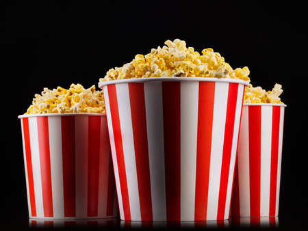 Paper striped buckets with popcorn isolated on black background, concept of watching TV or cinema.の写真素材