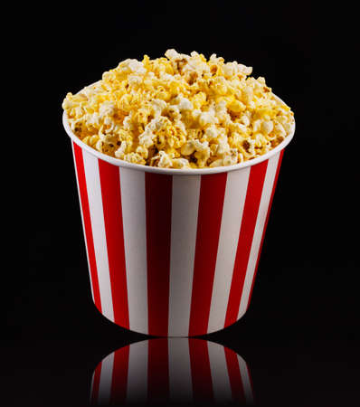 Paper striped bucket with popcorn isolated on black background, concept of watching TV or cinema.の写真素材