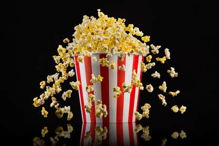 Flying popcorn from paper striped bucket isolated on blackの写真素材