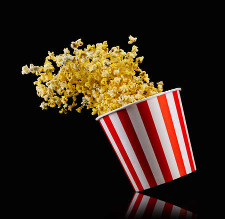 Flying popcorn from paper striped bucket isolated on black background, concept of watching TV or cinema.の写真素材