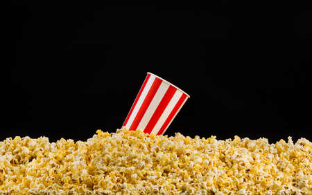 Paper striped bucket installed on scattered popcorn isolated on black background, concept of...