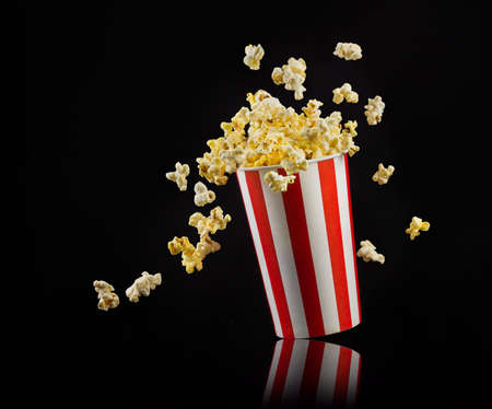 Flying popcorn from paper striped bucket isolated on black background, concept of watching TV or cinema.の写真素材