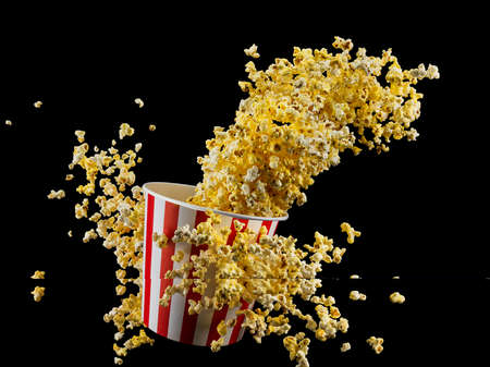 Flying popcorn from paper striped bucket isolated on black background, concept of watching TV or...
