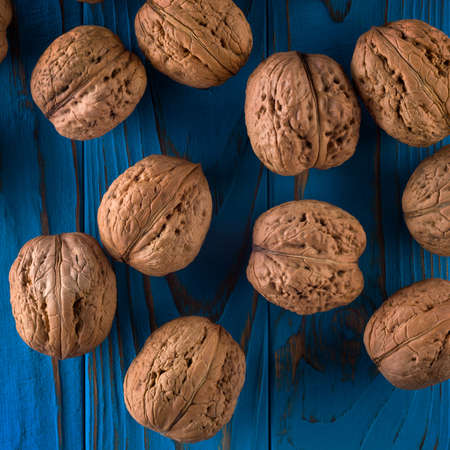 Top view photo of whole walnuts on painted blue wooden table in bowl.