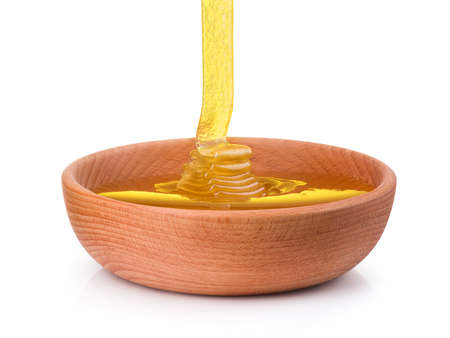 Wooden bowl full of honey and falling jet of honey on wooden plank isolated on white background with clipping path. Bee products by organic natural ingredients conceptの写真素材