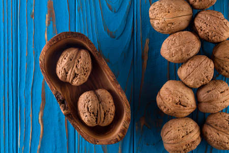 Whole walnuts on painted blue wooden table in bowl.の写真素材