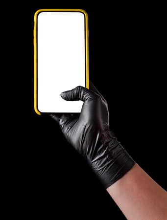 Hand in black glove holding mobile phone with blank screen on black background.の写真素材