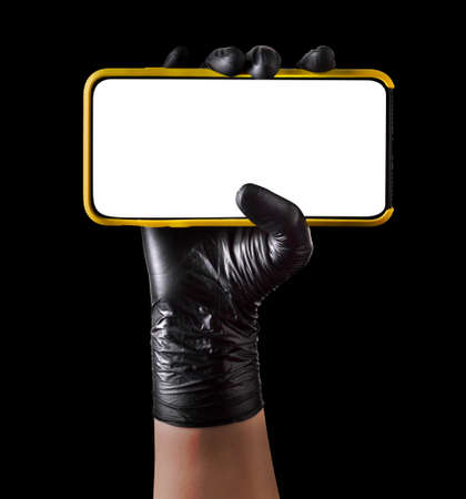 Hand in black glove holding mobile phone with blank screen on black background.