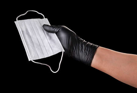 Hand in black gloves hold disposable face mask isolated on black background