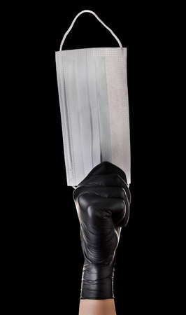 Hand in black gloves hold disposable face mask isolated on black backgroundの写真素材