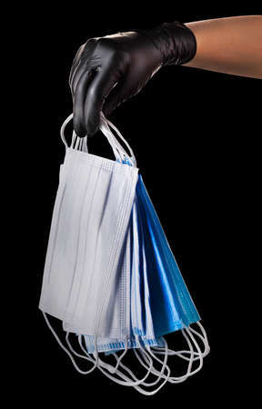 Hand in black gloves hold heap of face mask isolated on black