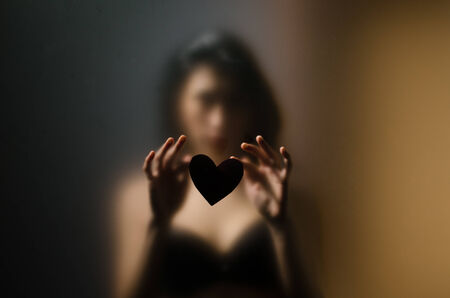 silhouette of young girl for sexual opaque glass with paper heart in handsの写真素材