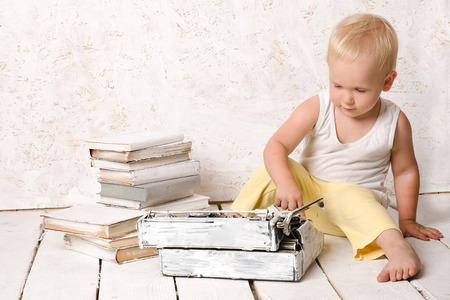 Boy sitting near retro typewriter and books on white painted floorの写真素材