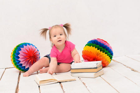 baby girl sitting on wooden dyed white floor near multicolored balls and booksの写真素材