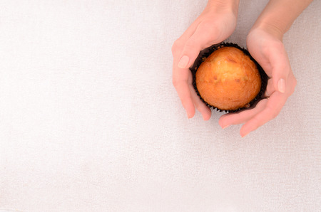 female hands with french manicure holding appetizing muffin on fabric backgroundの写真素材