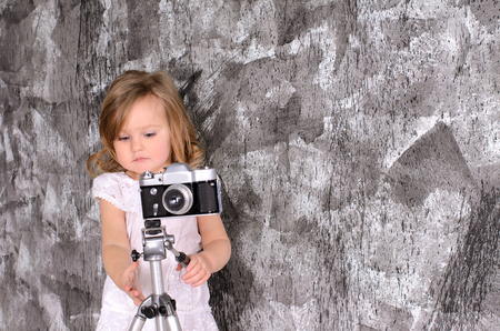 cute little girl investigating retro camera on rack on gray wall backgroundの写真素材
