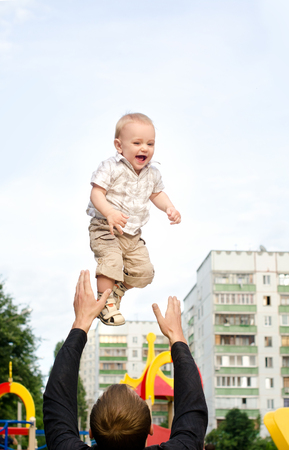 daddy tossing his infant son up on sky background in city outdoorsの写真素材