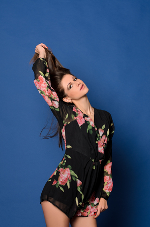 young woman with makeup in mini dress holding her hair and posing on blue studio backgroundの写真素材