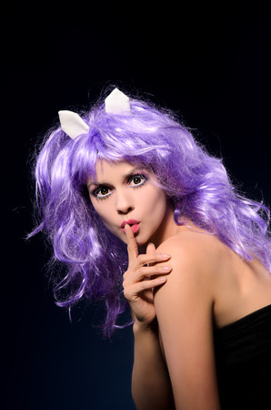 cosplay girl with makeup in purple wig showing sign be silent on dark studio backgroundの写真素材