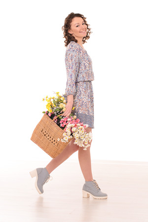 smiling pretty young woman with wavy hair going with bag of flowers on white studio backgroundの写真素材