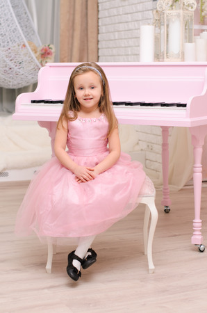 sitting little girl in evening gown and black shoes near opened pink grand piano indoorsの写真素材